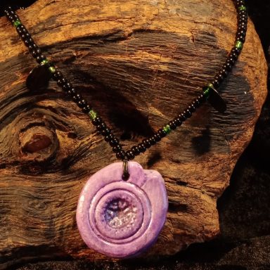 MÉMOIRES Pendentif violet en forme de spirale suspendu à un collier noir et vert.