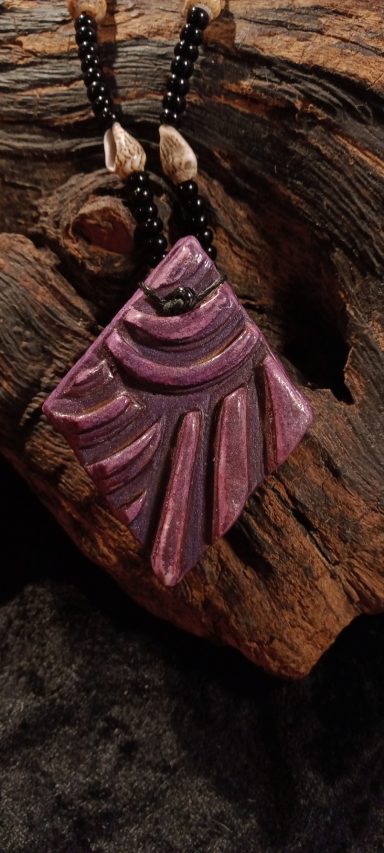 CAURI Pendentif en relief rose avec des perles noires suspendu sur un fond en bois.